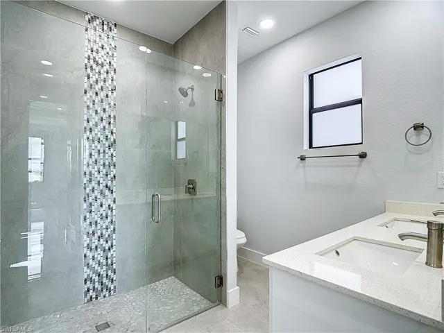 Bathroom with a shower with shower door, tile floors, toilet, and dual bowl vanity