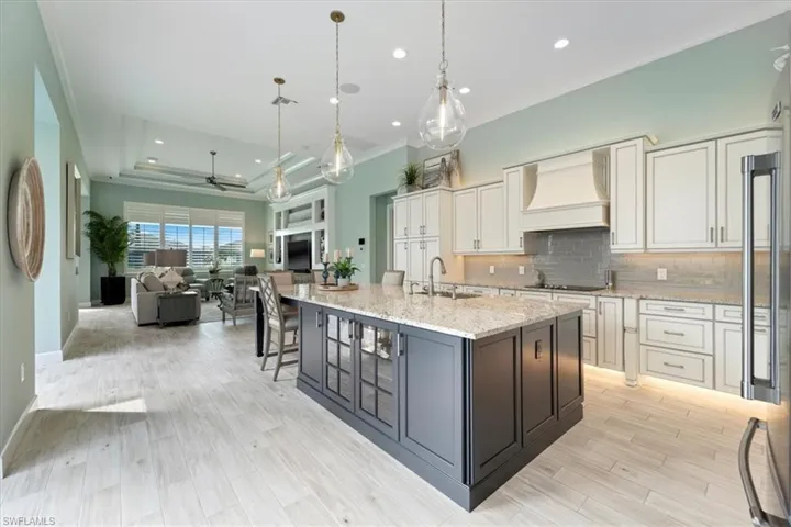 Kitchen with open floor plan, custom exhaust hood, decorative backsplash, black appliances, and a raised ceiling