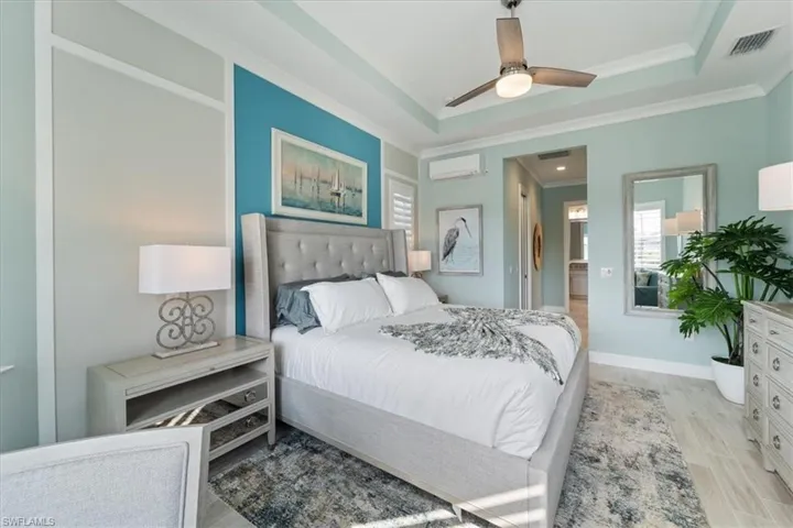 Bedroom with a tray ceiling, crown molding, light wood-style floors, an AC wall unit, and baseboards