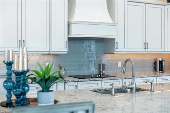 Kitchen featuring white cabinets, decorative backsplash, light stone counters, premium range hood, and a sink