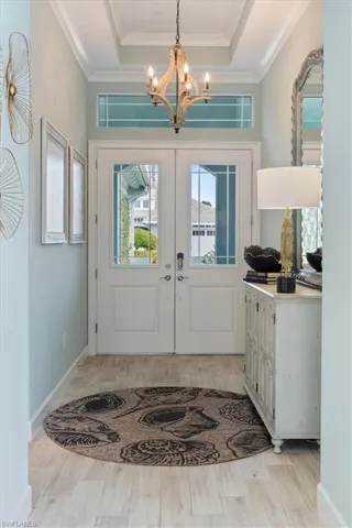 Entrance foyer with a chandelier, baseboards, french doors, ornamental molding, and a raised ceiling