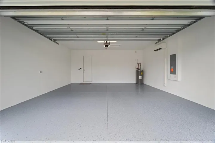 Garage featuring a garage door opener, electric panel, electric water heater, and a wall mounted AC