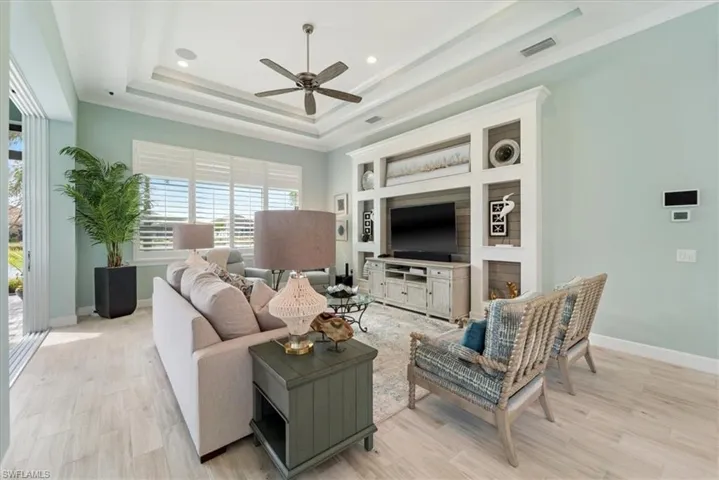 Living area with visible vents, baseboards, light wood finished floors, ornamental molding, and a tray ceiling