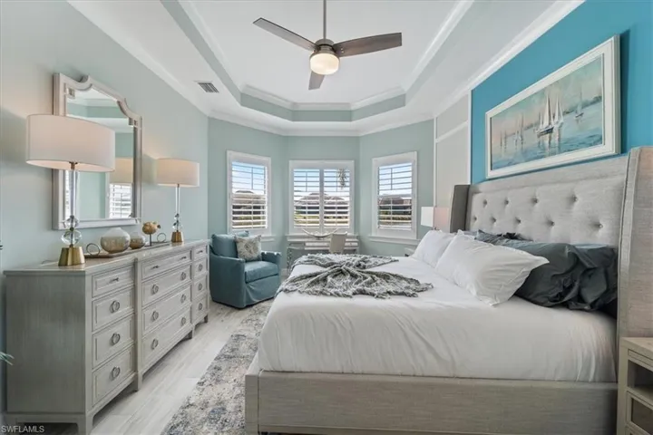 Bedroom featuring visible vents, a raised ceiling, ceiling fan, crown molding, and light wood-type flooring