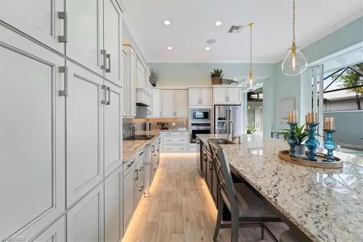 Kitchen with visible vents, light stone counters, stainless steel appliances, pendant lighting, and a sink