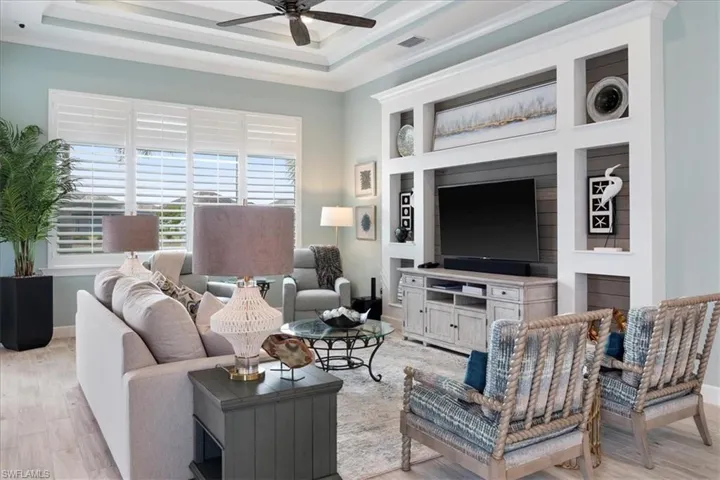 Living room featuring light wood-style floors, a raised ceiling, visible vents, and ceiling fan