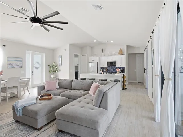 Living area with a barn door, vaulted ceiling, light flooring, and a ceiling fan