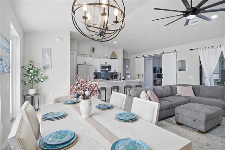 Dining area featuring a barn door, vaulted ceiling, ceiling fan, a chandelier, and recessed lighting