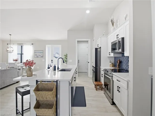 Kitchen featuring white cabinetry, an island with sink, a breakfast bar, appliances with stainless steel finishes, and pendant lighting