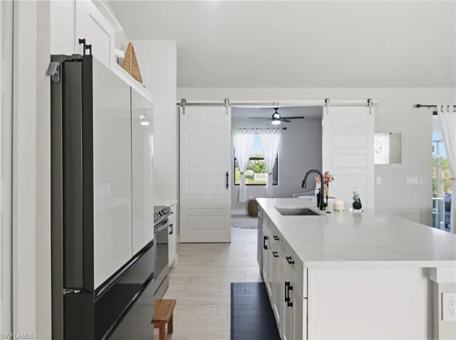 Kitchen featuring white cabinetry, freestanding refrigerator, light quartz countertops, an island with sink, and ceiling fan