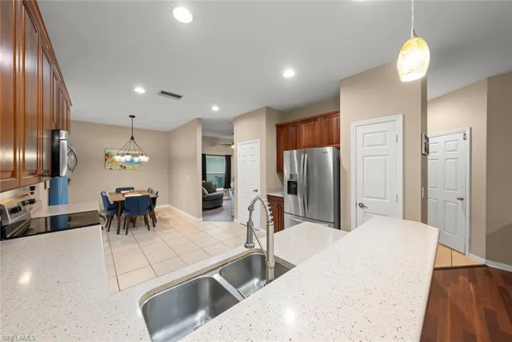 Kitchen with hanging light fixtures, stainless steel appliances, light counters, and wood finish cabinetry
