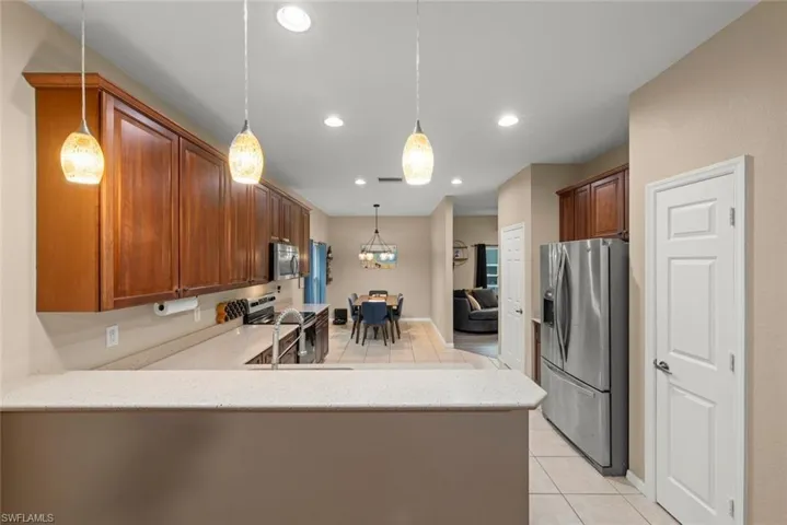 Kitchen featuring stainless steel appliances, light counters, light tile patterned floors, a peninsula, and wood finish cabinetry