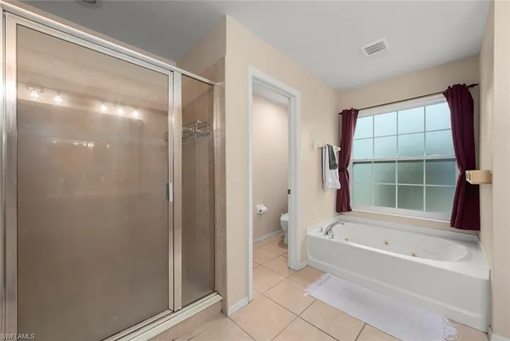 Primary bathroom featuring a shower stall, light tile patterned floors, a toilet closet, and a tub with jets