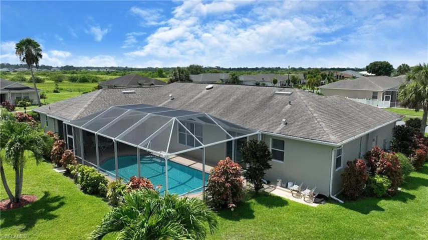 Back of house with an outdoor pool, a shingled roof, stucco siding, a patio, and a lawn