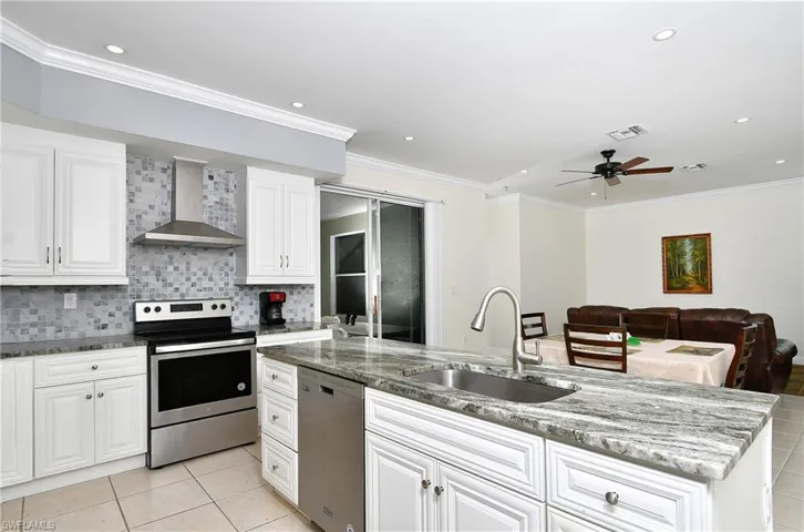 Kitchen featuring stainless steel appliances, wall chimney range hood, light tile patterned floors, crown molding, and ceiling fan