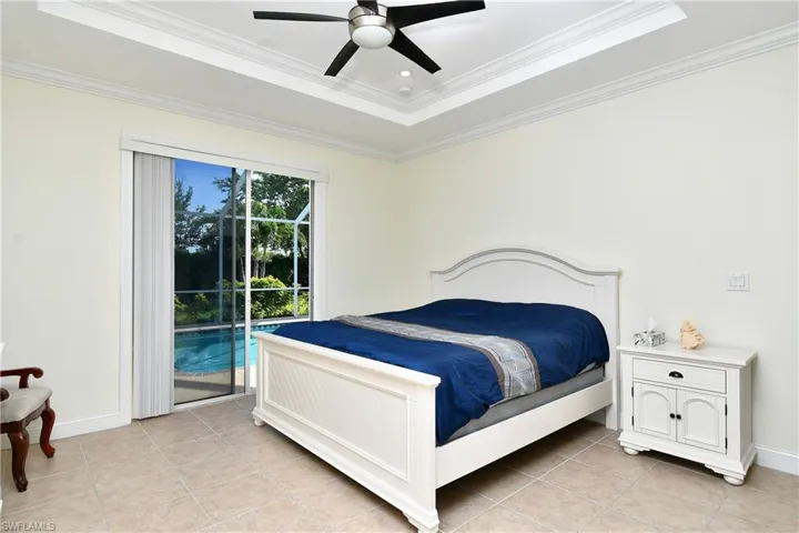 Bedroom with access to exterior, light tile patterned floors, ornamental molding, a raised ceiling, and a ceiling fan