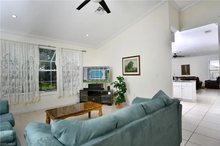 Living room featuring ceiling fan, light tile patterned flooring, crown molding, recessed lighting, and lofted ceiling