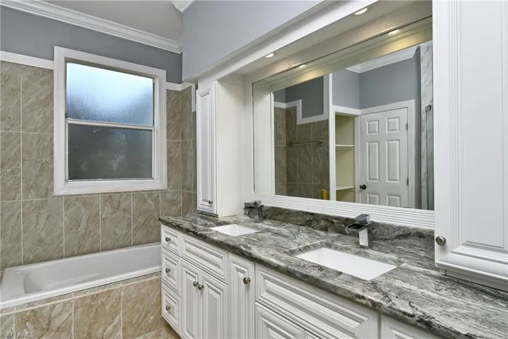 Bathroom with double vanity, tiled tub, ornamental molding, and a tile shower