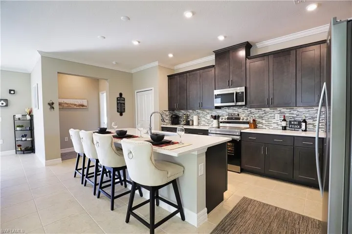 Kitchen with stainless steel appliances, ornamental molding, dark brown cabinets, decorative backsplash, and light countertops