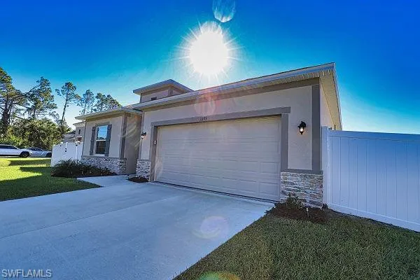 View of front of home featuring stone siding, driveway, a garage, stucco siding, and a front yard