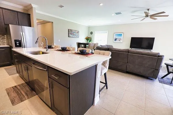 Kitchen with stainless steel appliances, a kitchen bar, light tile patterned floors, dark brown cabinets, and ornamental molding