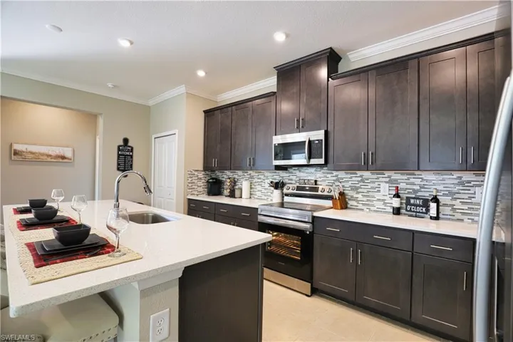 Kitchen with appliances with stainless steel finishes, crown molding, tasteful backsplash, a kitchen island with sink, and dark brown cabinets