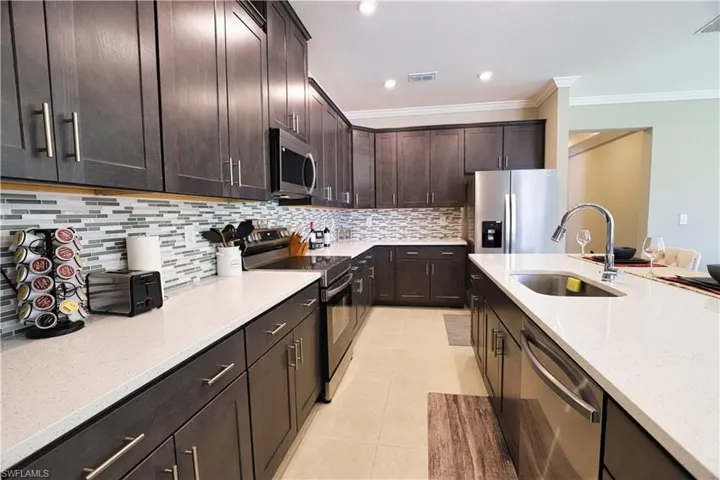 Kitchen featuring appliances with stainless steel finishes, a breakfast bar, an island with sink, backsplash, and light tile patterned floors