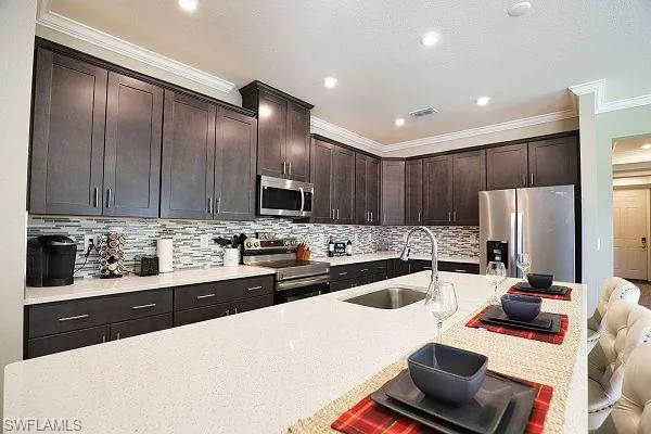 Kitchen with stainless steel appliances, ornamental molding, decorative backsplash, dark brown cabinets, and light countertops