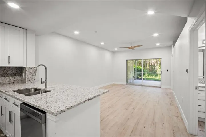 Kitchen featuring white cabinetry, backsplash, light stone countertops, stainless steel dishwasher, and recessed lighting