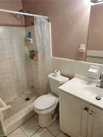 Bathroom featuring tile walls, vanity, a stall shower, and wainscoting