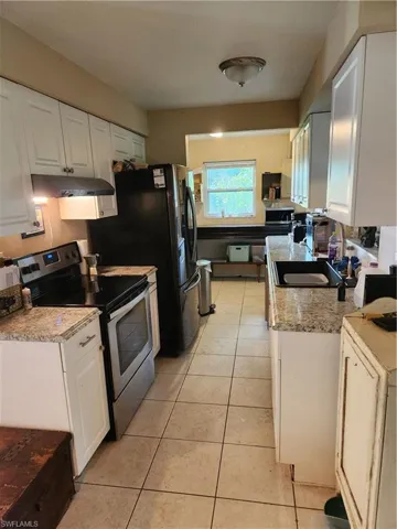 Kitchen with range, exhaust hood, white cabinets, and light tile patterned flooring