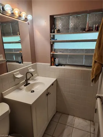 Bathroom with tile walls, vanity, a wainscoted wall, and marble look tiles