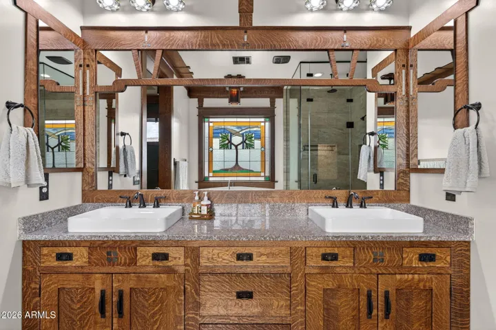 The primary bath offers dual sinks, granite countertops, and beautiful custom wood cabinetry. Overlooking the lush backyard, this updated bathroom highlights craftsmanship and modern comfort in this move-in-ready Phoenix home.