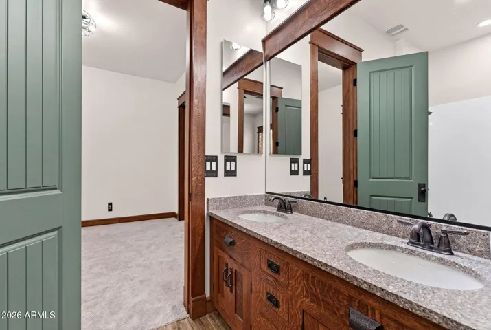 This dual-sink vanity connects two bedrooms in the Jack & Jill layout and features custom oak cabinetry, granite counters, and vintage-inspired fixtures—perfect for shared living with style and functionality in Phoenix.