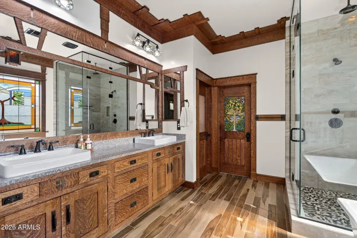 This spa-worthy bathroom boasts a dual vanity, stained-glass windows, a freestanding tub, and walk-in glass shower. Elegant finishes create a peaceful retreat in North Phoenix.
