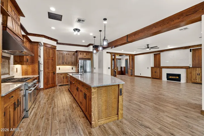 This open-concept space seamlessly unites the chef’s kitchen and living room, featuring exposed beams, a statement island, and a gas fireplace—ideal for entertaining in your Phoenix home.