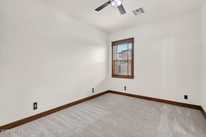This well-sized bedroom features soft green walls, wood trim, and natural light—perfect for a serene workspace, nursery, or guest accommodation in your Phoenix property.