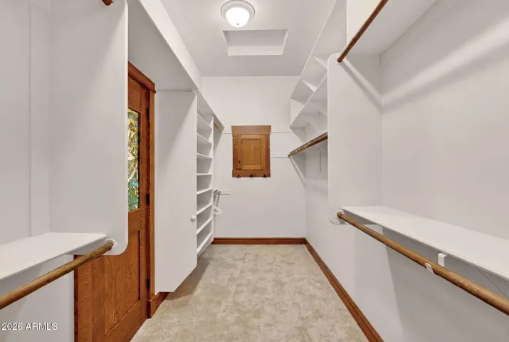 This spacious walk-in closet features built-in shelving, plush carpet, and a door accented by a colorful stained glass panel. A perfect blend of function and style in this thoughtfully designed home in Phoenix, AZ.