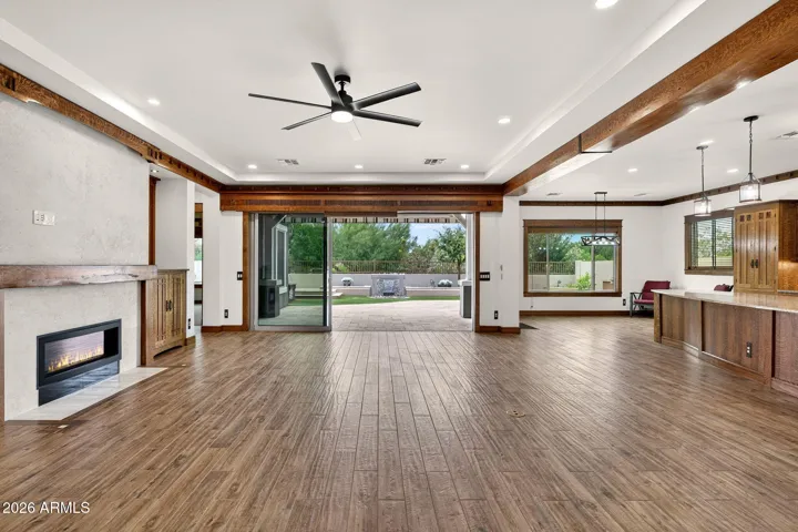 The open-concept living area features hardwood-look porcelain tile, decorative beams, and Craftsman-era lighting. Abundant natural light enhances the Arizona indoor-outdoor lifestyle.