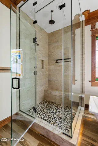 The primary bath features a custom walk-in shower with pebble-stone flooring, a bench seat, and a sleek frameless glass door—combining comfort and design in this upgraded Craftsman home.