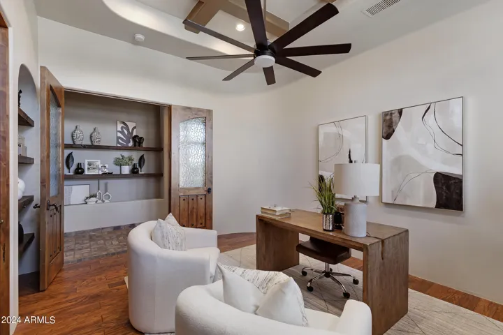 The full sized den at the front of the homes boasts double doors with glass inserts, wood floors, beamed ceiling and wood shelving.