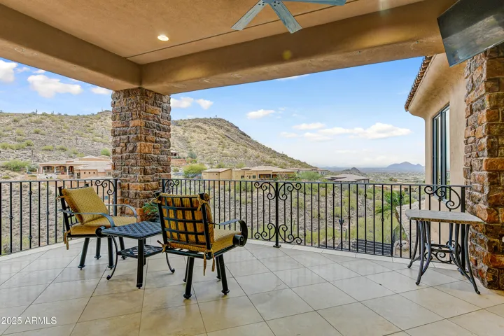 Enjoy sweeping views of the desert hills and distant mountains from this covered balcony, ideal for shaded relaxation. The spacious tile flooring and wrought iron railing pair beautifully with the natural stone accents, creating an outdoor space perfect for unwinding or entertaining in this elevated Arizona retreat.