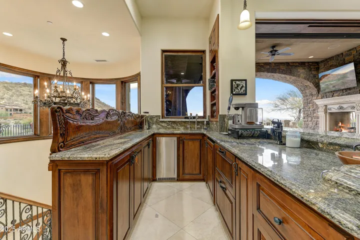 A fully equipped wet bar with custom woodwork, granite counters, kegerator, beverage fridge, and sink—perfectly positioned near the patio with views of the Arizona desert landscape.