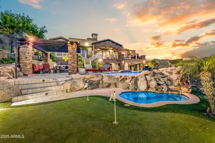 Showcasing the breathtaking backyard oasis of this Scottsdale luxury home, complete with a solar-heated dive pool, elevated spa, natural rock waterfall, pergola-covered seating, and putting green—all set against Camelback Mountain and city light views.