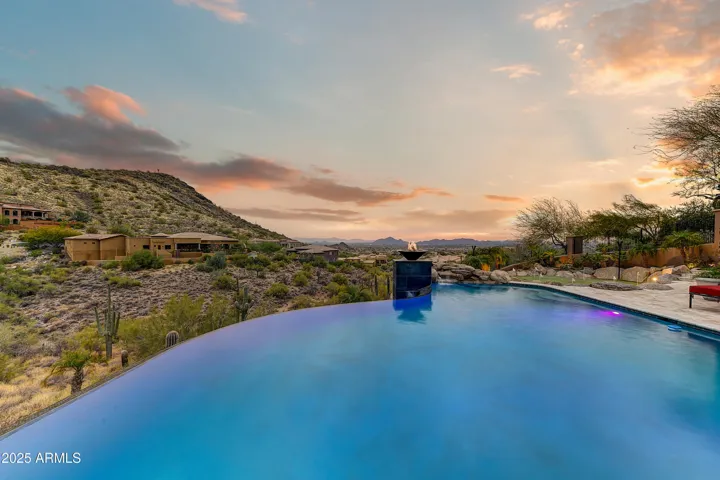 The stunning negative-edge pool seemingly melts into the desert landscape, creating a seamless visual connection to the distant mountain peaks. Fire bowls add ambient light to this luxury oasis, elevating every evening swim into a scenic experience.