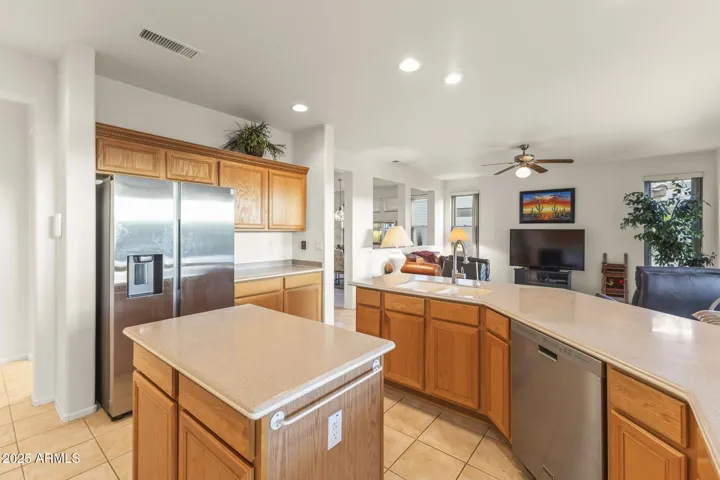 Seamless flow between the kitchen and living area, with bright recessed lighting, stainless refrigerator, and warm cabinetry creating a welcoming Arizona ambiance.