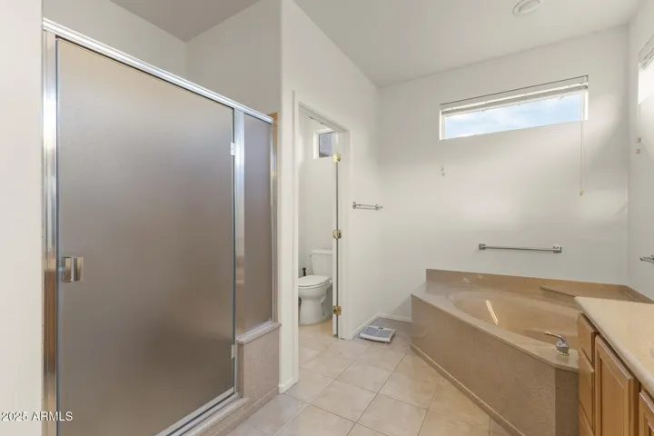 Primary bathroom with a frosted-glass shower, deep soaking tub, and bright tile floors, offering functionality and comfort in a clean, modern layout.
