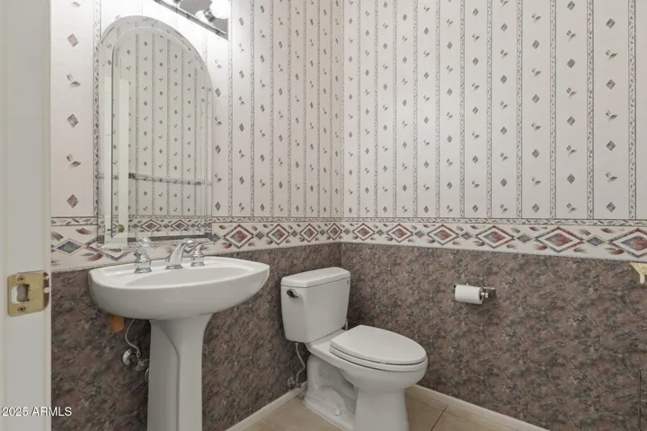 Stylish powder room with pedestal sink, framed mirror, and decorative wallpaper accents, offering charm and convenience for visitors.