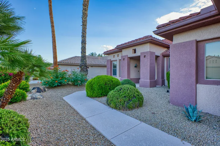 Inviting walkway lined with lush palms and colorful blooms leading to a beautifully maintained entrance that enhances the home’s desert curb appeal.