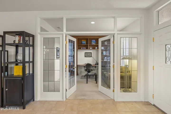 Elegant glass-paneled French doors lead to a bright den with custom built-ins, perfect for a home office or reading retreat in this Surprise golf course home.